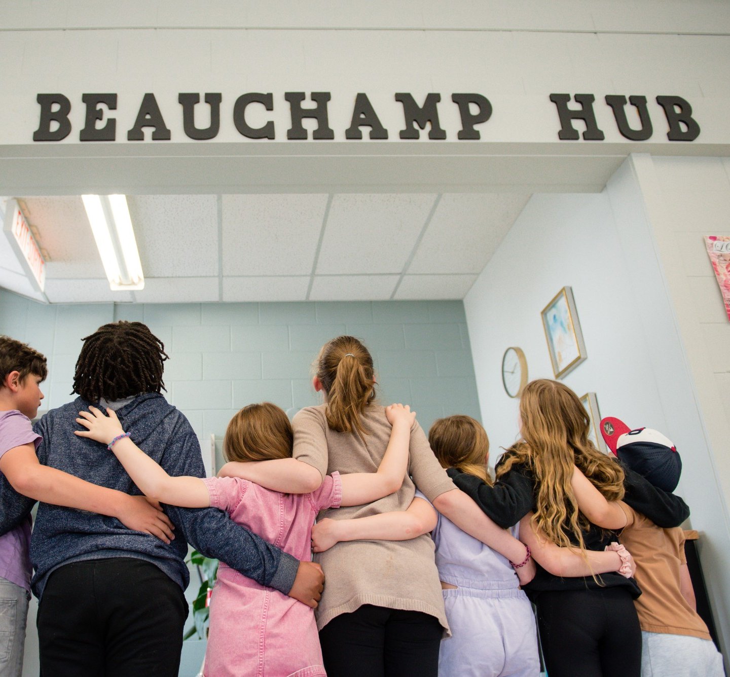 Children standing with their arms around each other beneath the Beauchamp Hub sign
