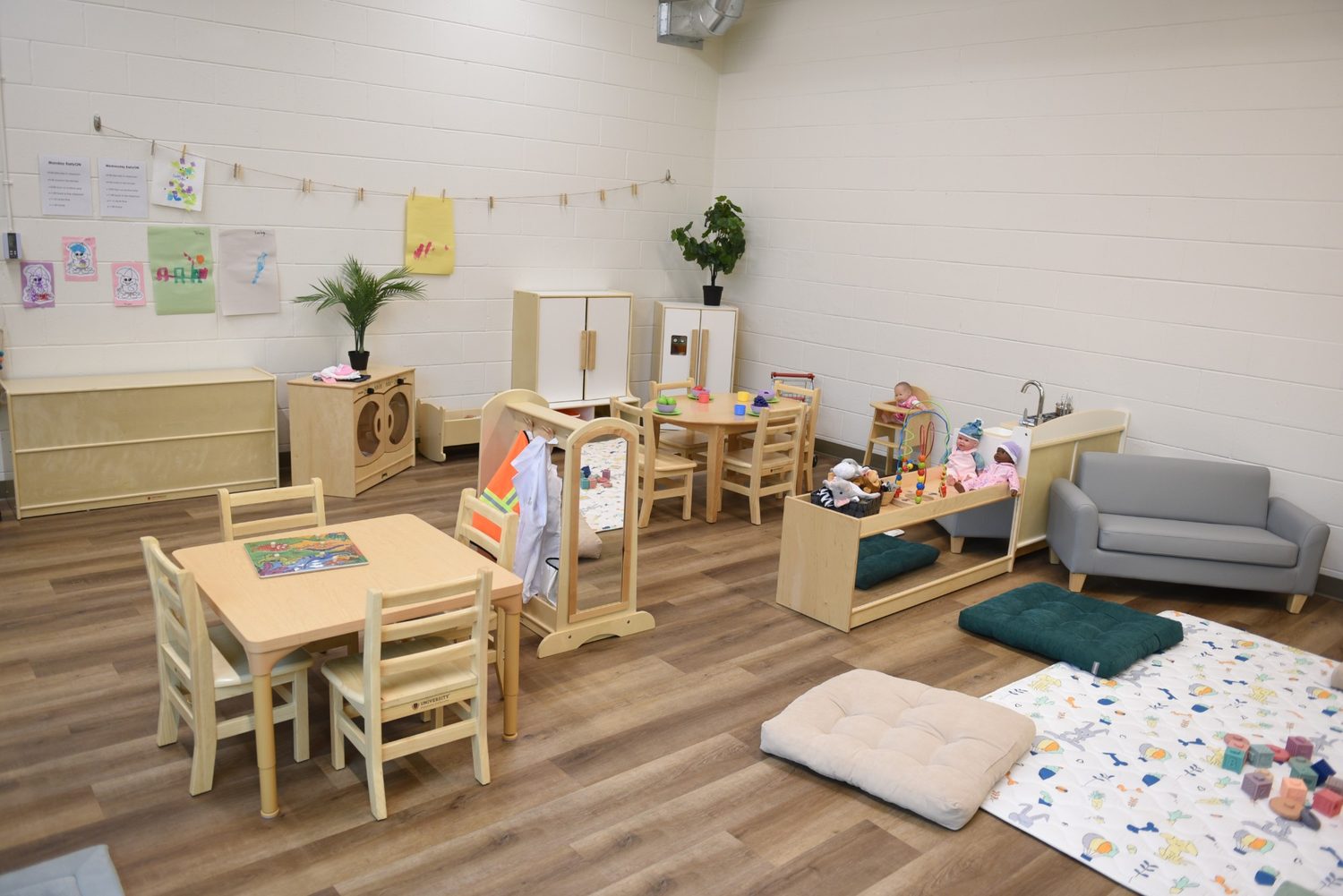 A bright on-site room with child-sized tables and chairs, play areas and children’s artwork
